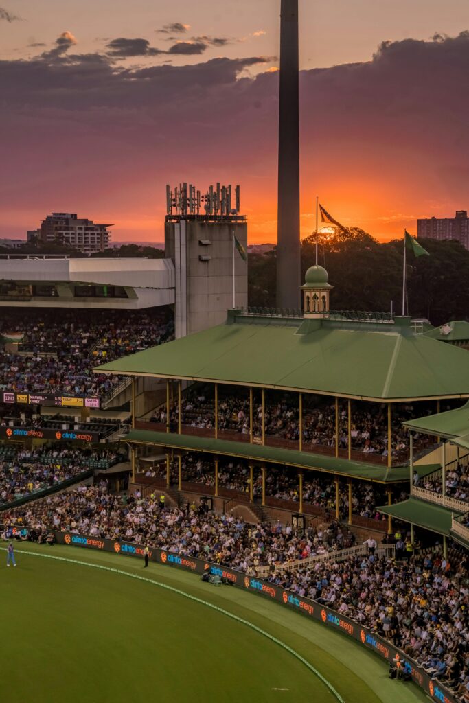 A colorful sunset over a bustling cricket stadium, capturing the lively atmosphere of the event.